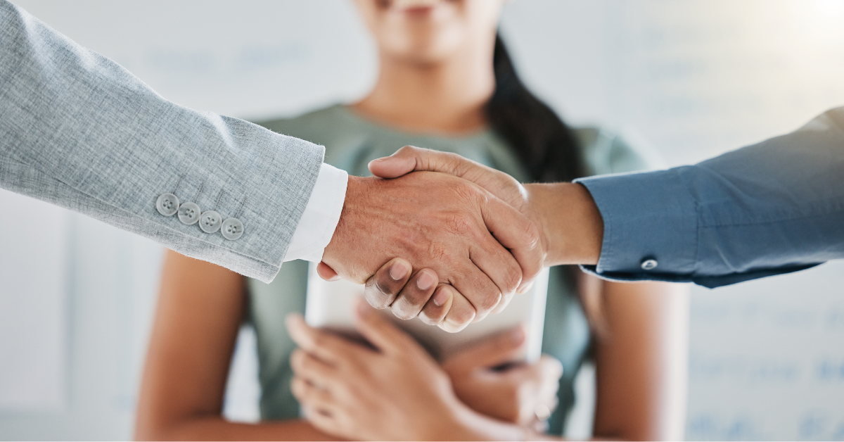 Datatronic_Karriereblog_Mitarbeiter-Onboarding - So gelingt der perfekte Einstieg ins Team!_IT Karriere_eine Frau in Bürokleidung im Hintergrun zwei Männerhände die sich die Hand geben 